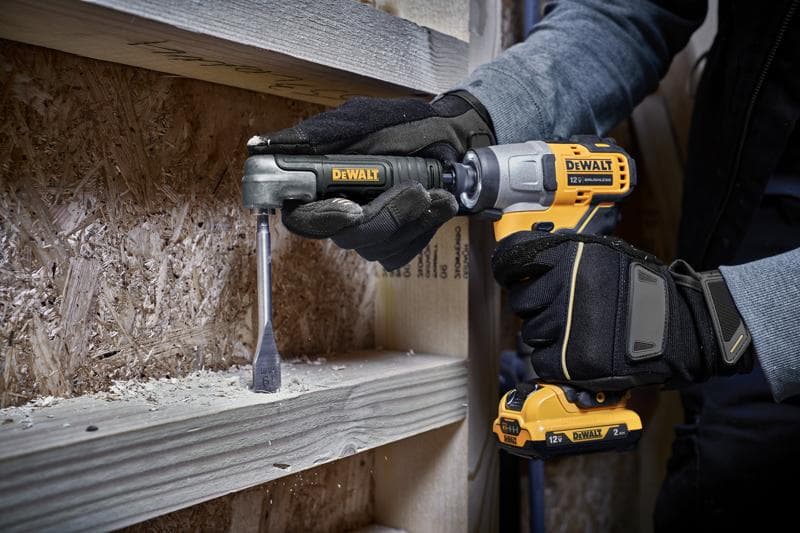 Eine Person mit Handschuhen benutzt einen DEWALT 12V Akku-Bohrer mit einem rechten Winkelaufsatz, um ein Holzbrett zu bohren. Holzspäne sind um den Arbeitsbereich herum sichtbar.