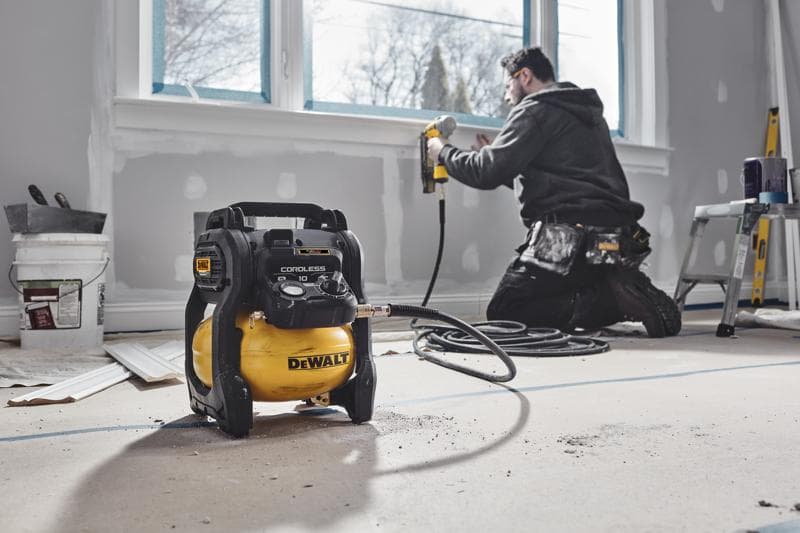 DEWALT kabelloser Kompressor im renovierten Raum, Arbeiter nutzt Nagelpistole am Fenster.