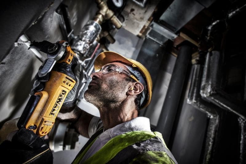 Arbeiter schneidet Rohr mit DEWALT DWE315, trägt Helm und Weste in industrieller Umgebung.