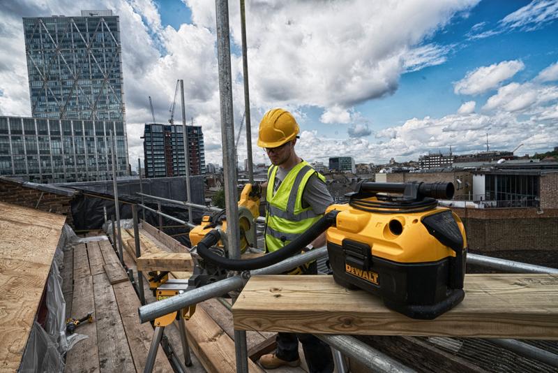 DEWALT DCV584 Sauger auf einer Baustelle mit einem Arbeiter und Stadtgebäuden im Hintergrund.