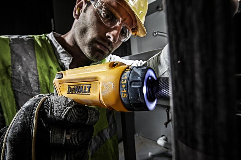 Person nutzt gelben DEWALT DCF680G2-Schraubendreher mit Handschuh in industrieller Umgebung.