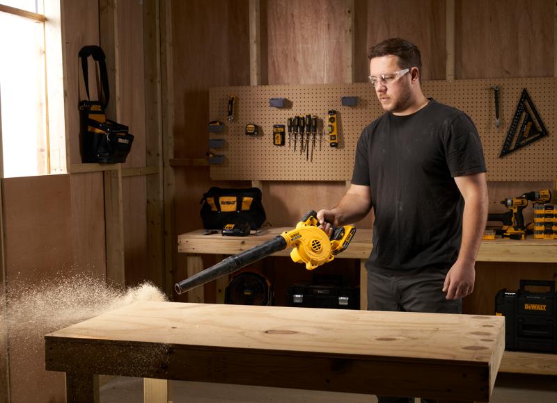 Person nutzt einen DEWALT DCV100 Bläser, um Sägemehl von einer Holzwerkbank in einer Werkstatt zu entfernen.